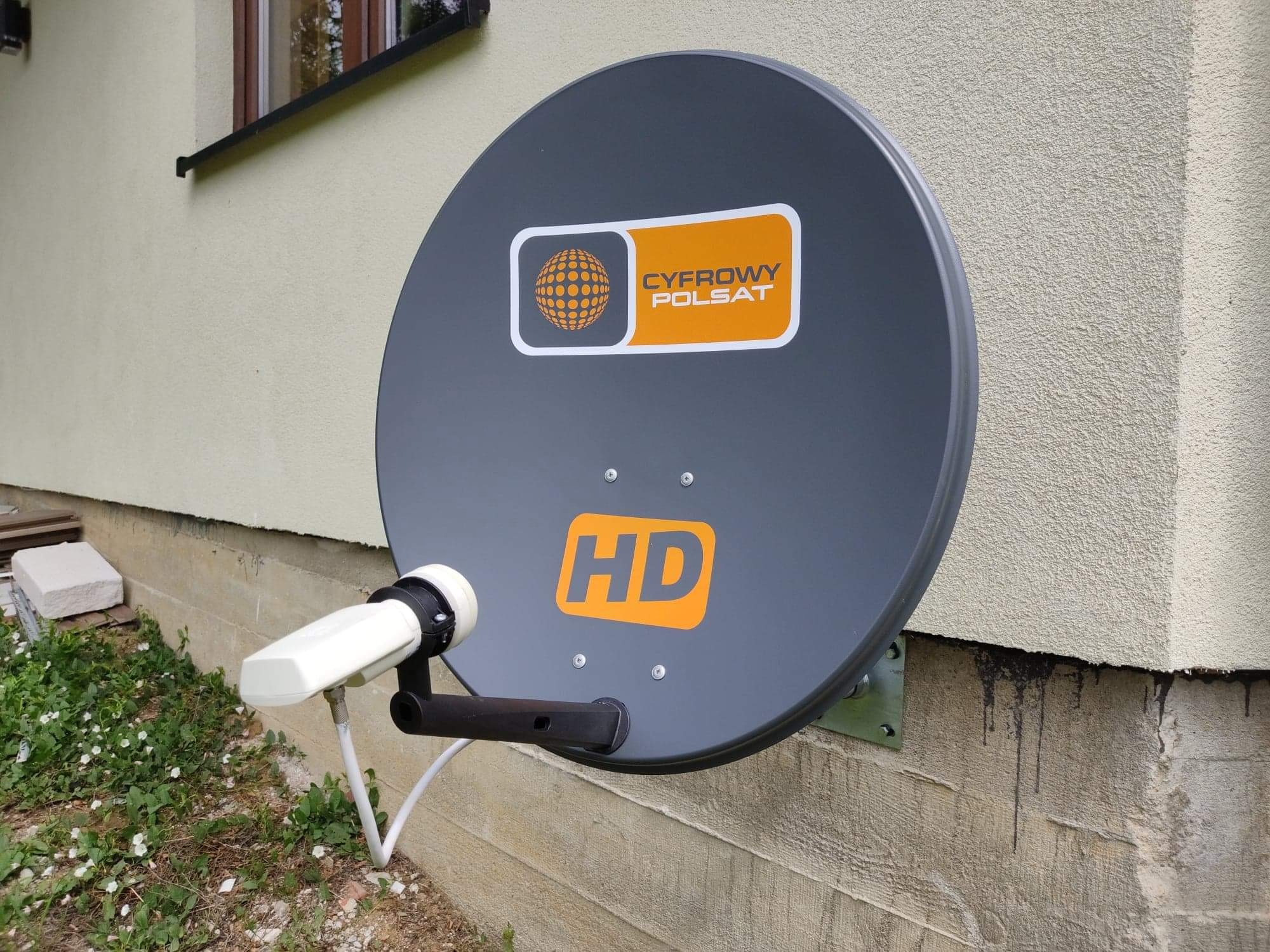 Szara antena satelitarna Cyfrowy Polsat HD zamontowana na elewacji budynku, widoczne mocowanie i przewody.