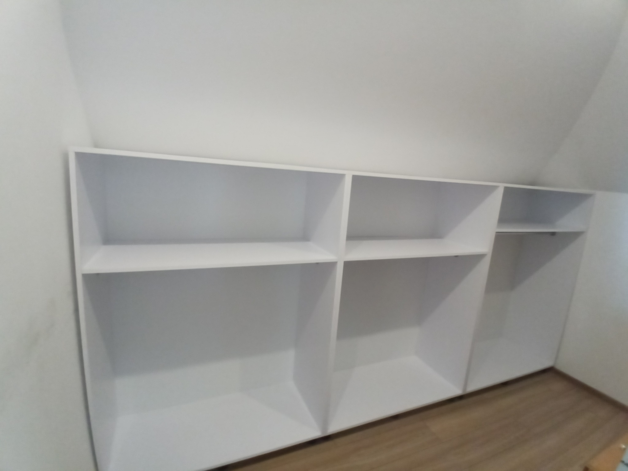 Biała, otwarta szafa wnękowa z półkami, zamontowana pod skosem dachu, widok z dołu.