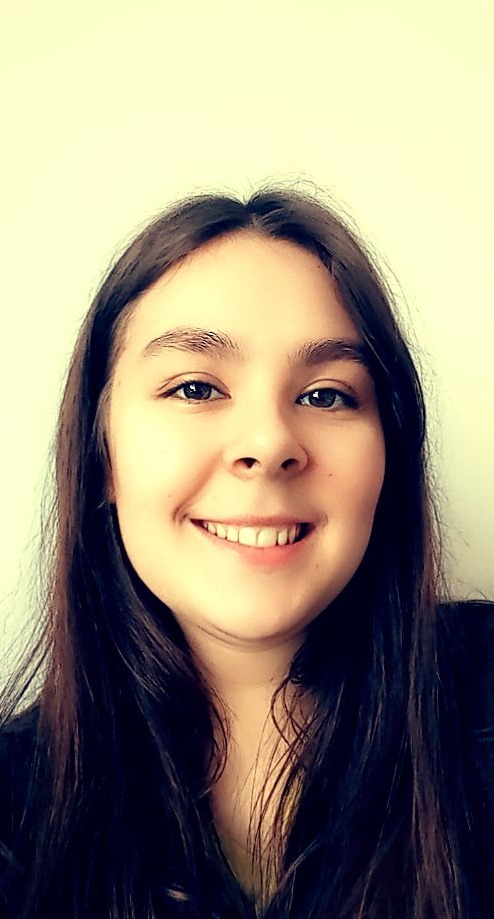 Portret uśmiechniętej kobiety z długimi, ciemnymi włosami na jasnym tle.