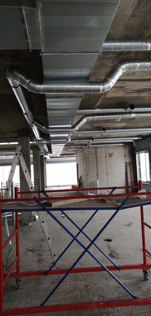 Montaż kanałów wentylacyjnych prostokątnych i okrągłych pod betonowym stropem, widoczne rusztowanie i drabina.