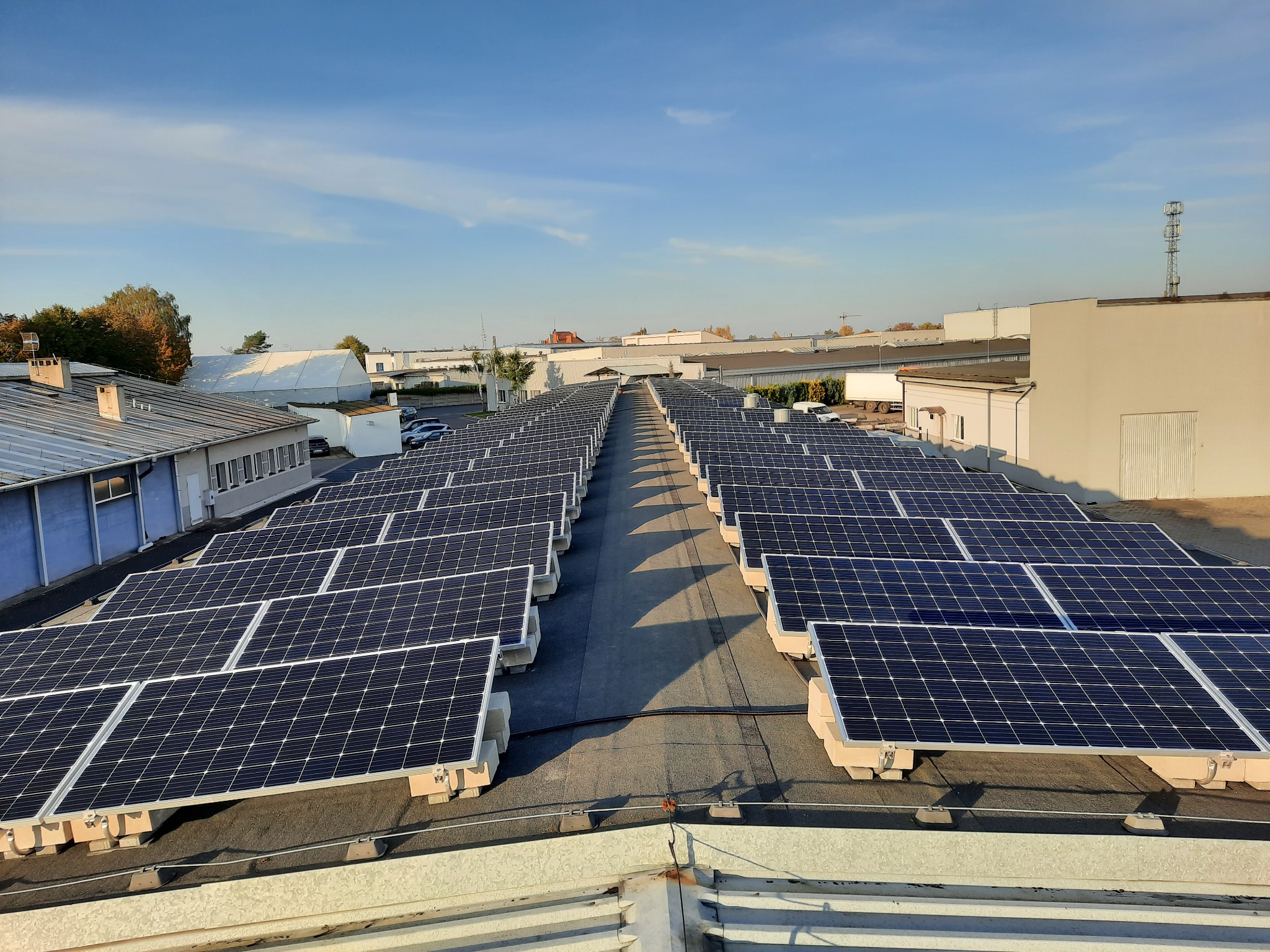 Rząd paneli słonecznych zamontowanych na płaskim dachu budynku przemysłowego, widok z góry w słoneczny dzień.