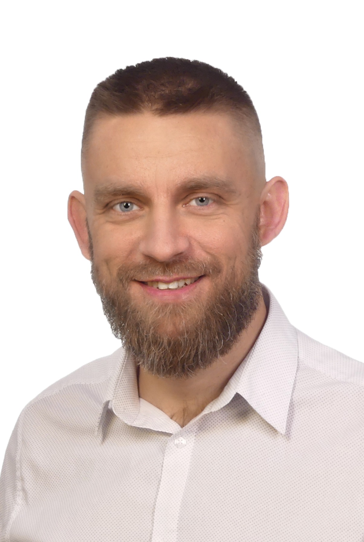 Portret uśmiechniętego mężczyzny z brodą na białym tle, ubrany w koszulę z delikatnym wzorem.