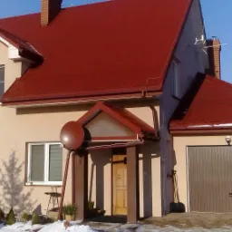 Dom jednorodzinny z czerwoną dachówką, antena satelitarna zamontowana przy wejściu, zimowy krajobraz z odśnieżonym podjazdem.