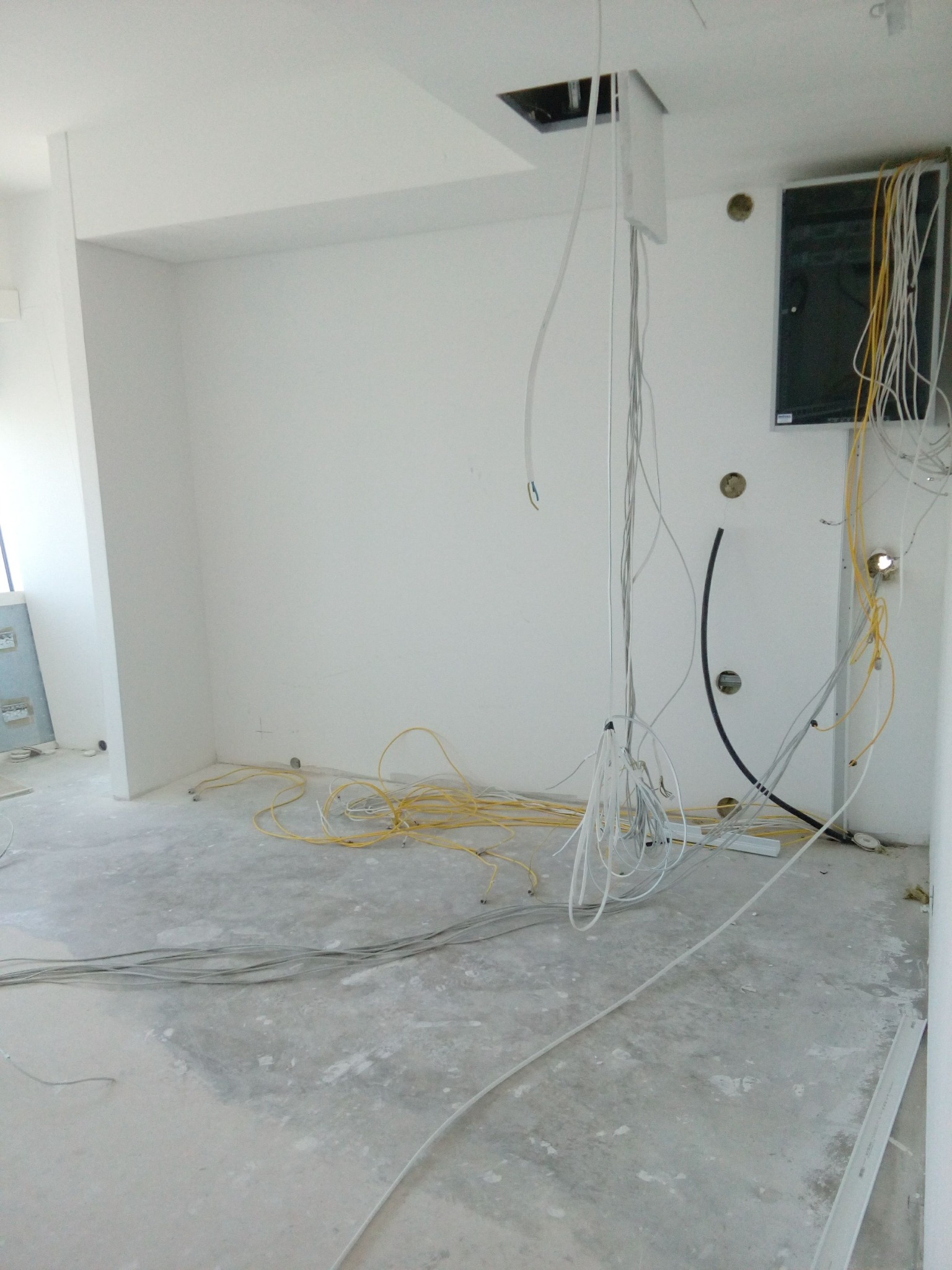 Surowy stan instalacji elektrycznej w jasnym pomieszczeniu: zwisające kable z sufitu, przewody na podłodze, puszki instalacyjne w ścianie.