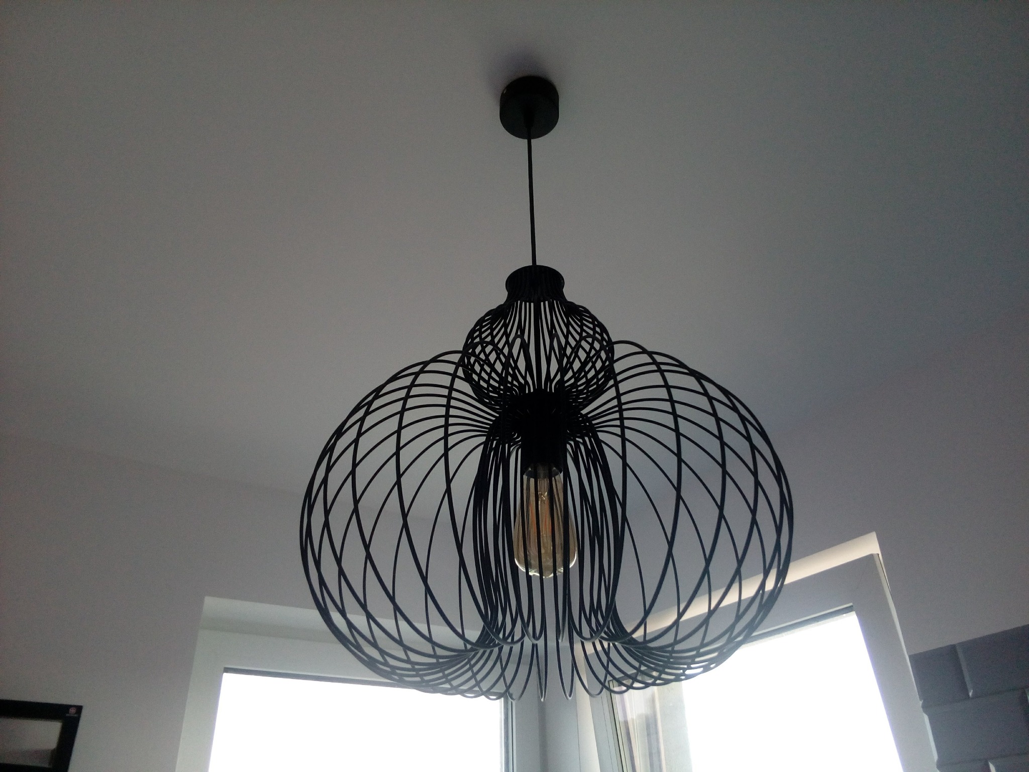 Czarna, metalowa lampa wisząca w stylu industrialnym z żarówką Edisona, zamontowana na białym suficie, widok z dołu.