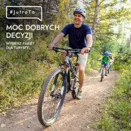 Uśmiechnięty mężczyzna w kasku rowerowym jedzie na rowerze górskim leśną ścieżką, w tle dwójka dzieci również na rowerach; hasło reklamowe 'MOC DOBRYCH DECYZJI. WYBIERZ PAKIET DLA TURYSTY.'
