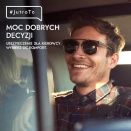 Uśmiechnięty mężczyzna w okularach przeciwsłonecznych siedzi za kierownicą samochodu, na szybie widoczny napis 'Moc dobrych decyzji. Ubezpieczenie dla kierowcy. Wybierz OC komfort.'