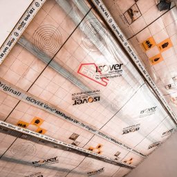 FRB Silesia - Izolacja poddasza folią paroizolacyjną Isover Vario KM Duplex UV z widocznymi nadrukami i taśmami uszczelniającymi na krawędziach, zamontowana w skosie dachu.