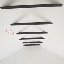 FRB Silesia - Biały sufit z dekoracyjnymi, ciemnymi belkami drewnianymi ułożonymi w perspektywie, widoczne logo firmy remontowo-budowlanej w lewym rogu.