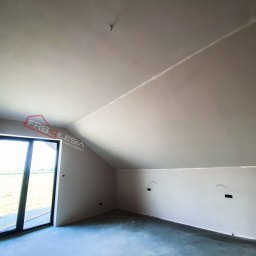 FRB Silesia - Poddasze po szpachlowaniu ścian i sufitu, widoczne gniazdka elektryczne bez osprzętu oraz okno z widokiem na zewnątrz.