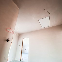 FRB Silesia - Wnętrze w trakcie prac wykończeniowych; ściany i sufit po szpachlowaniu, widoczny otwór rewizyjny w suficie, wystające kable, logo firmy na ścianie, przygotowane do dalszych prac.