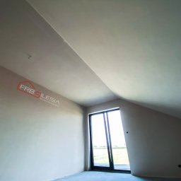FRB Silesia - Poddasze po gładziowaniu, widoczne ściany pomalowane na jasny kolor, okno balkonowe i fragment logo firmy na ścianie.