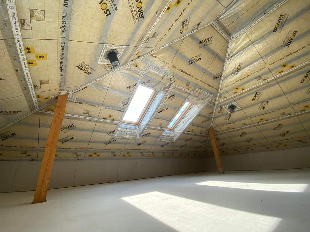 Poddasze po ociepleniu folią paroizolacyjną Isover Vario KM Duplex UV, widoczne okna dachowe i drewniane podpory, surowy stan wykończenia.