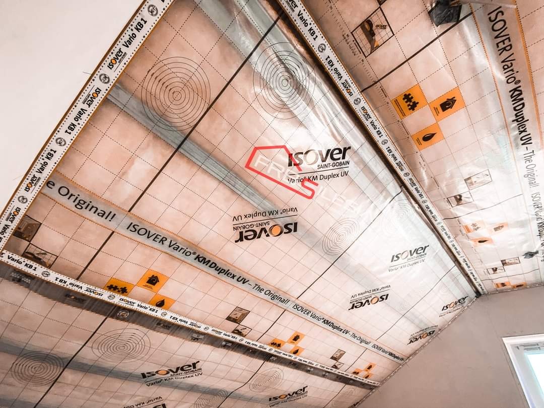 Izolacja poddasza folią paroizolacyjną Isover Vario KM Duplex UV z widocznymi nadrukami i taśmami uszczelniającymi na krawędziach, zamontowana w skosie dachu.