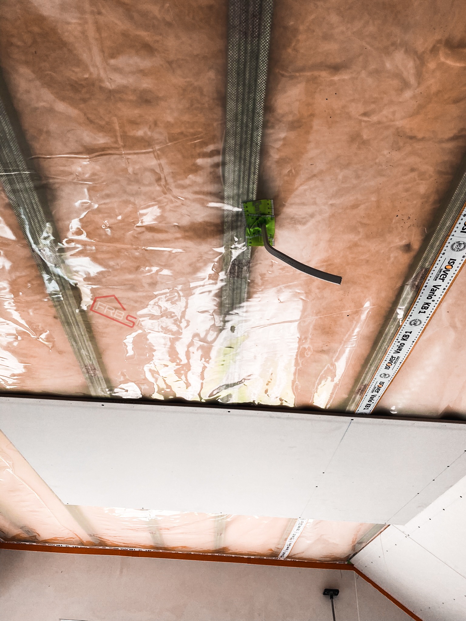 Montaż płyty karton gips na poddaszu z widoczną folią paroizolacyjną, metalowymi profilami i elementami mocującymi, z bliska widoczna taśma miernicza Isover Vario KB1.