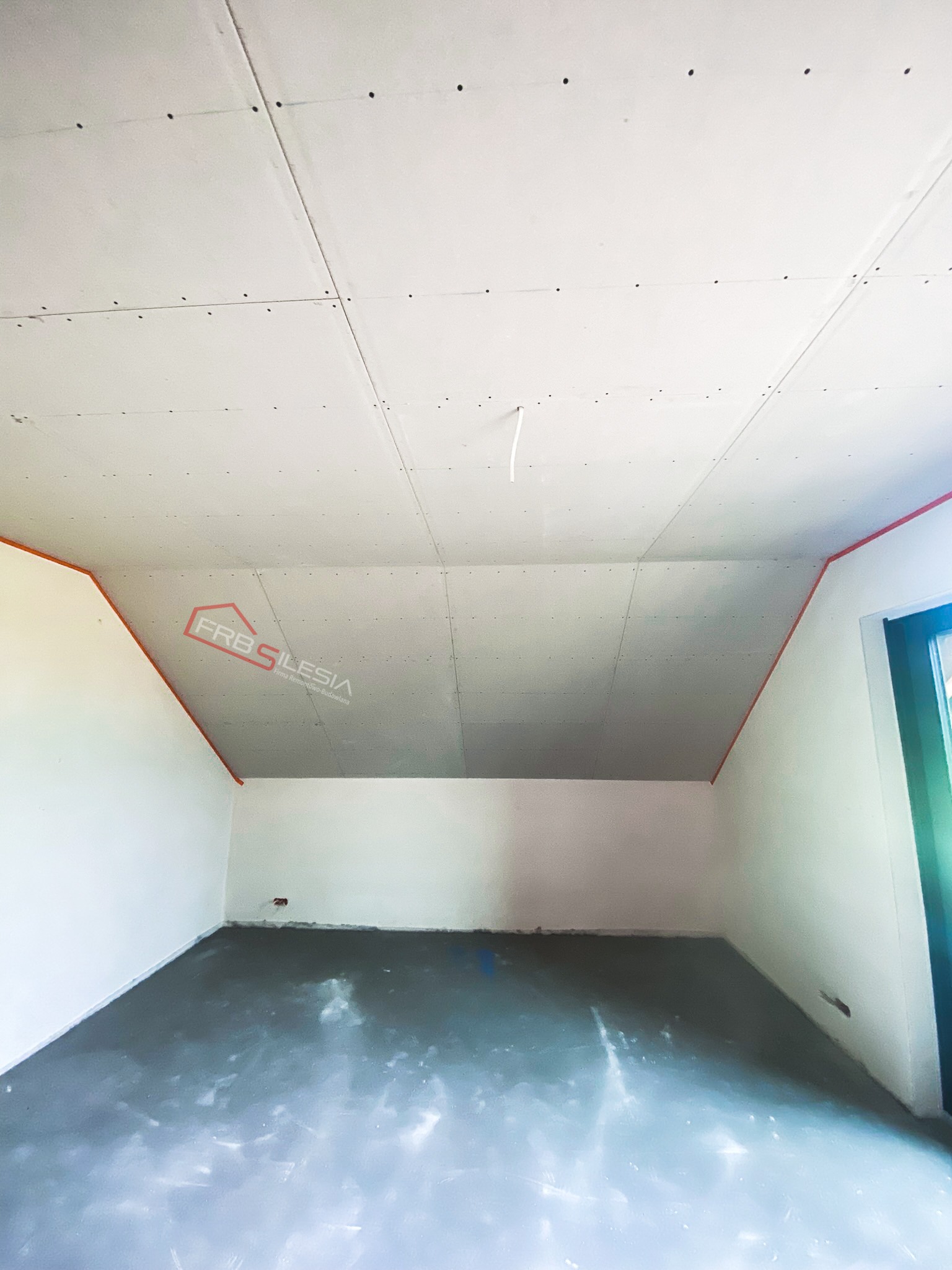 Poddasze z zamontowanymi płytami kartonowo-gipsowymi, widoczne łączenia płyt na skosach sufitu, szpachlowane otwory po wkrętach, surowa wylewka na podłodze, narożniki ścian zabezpieczone...