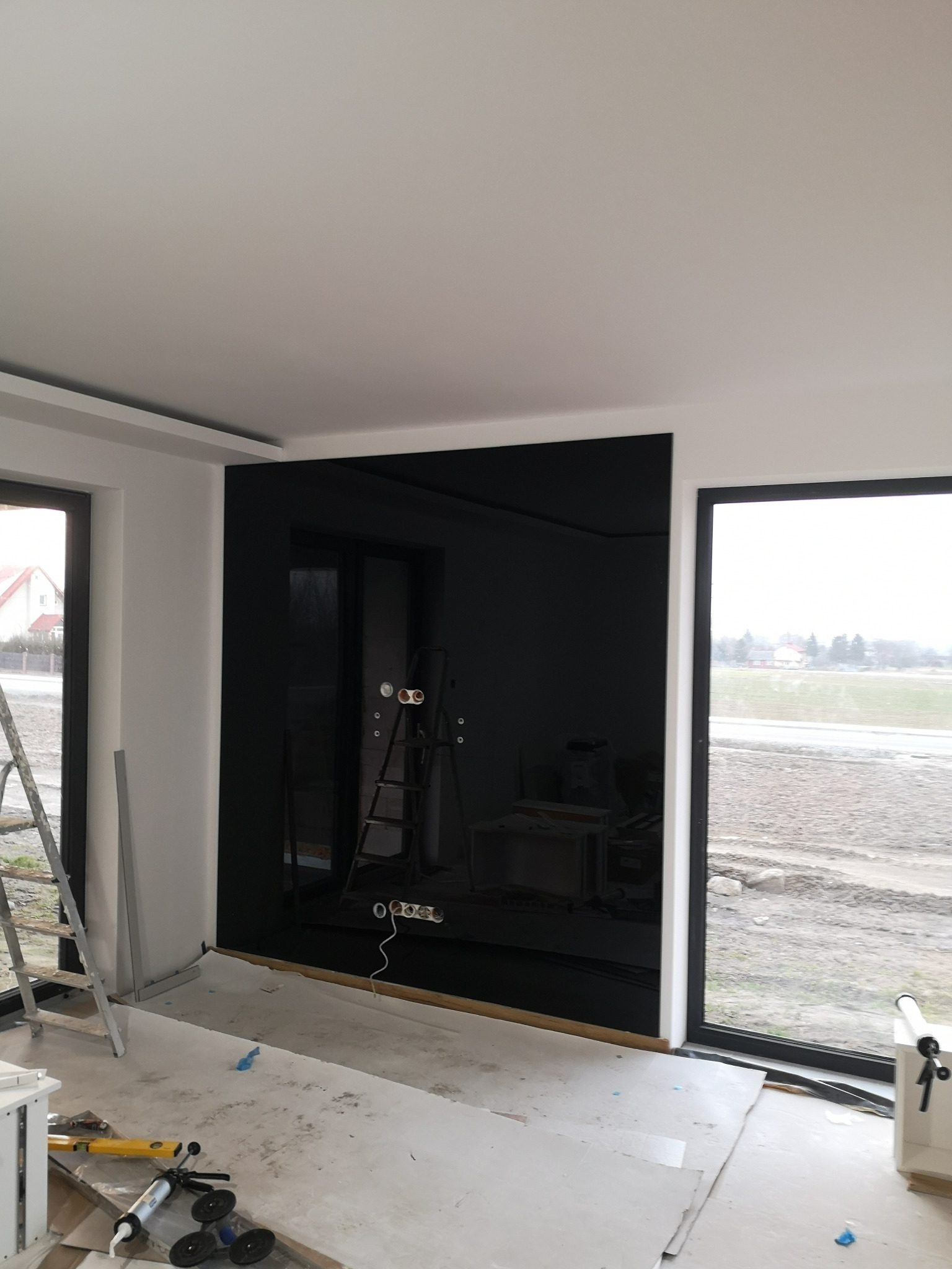 Czarne szkło lacobel zamontowane na ścianie w nowym budynku, widoczne puszki elektryczne i drabina, przygotowane do dalszych prac wykończeniowych.