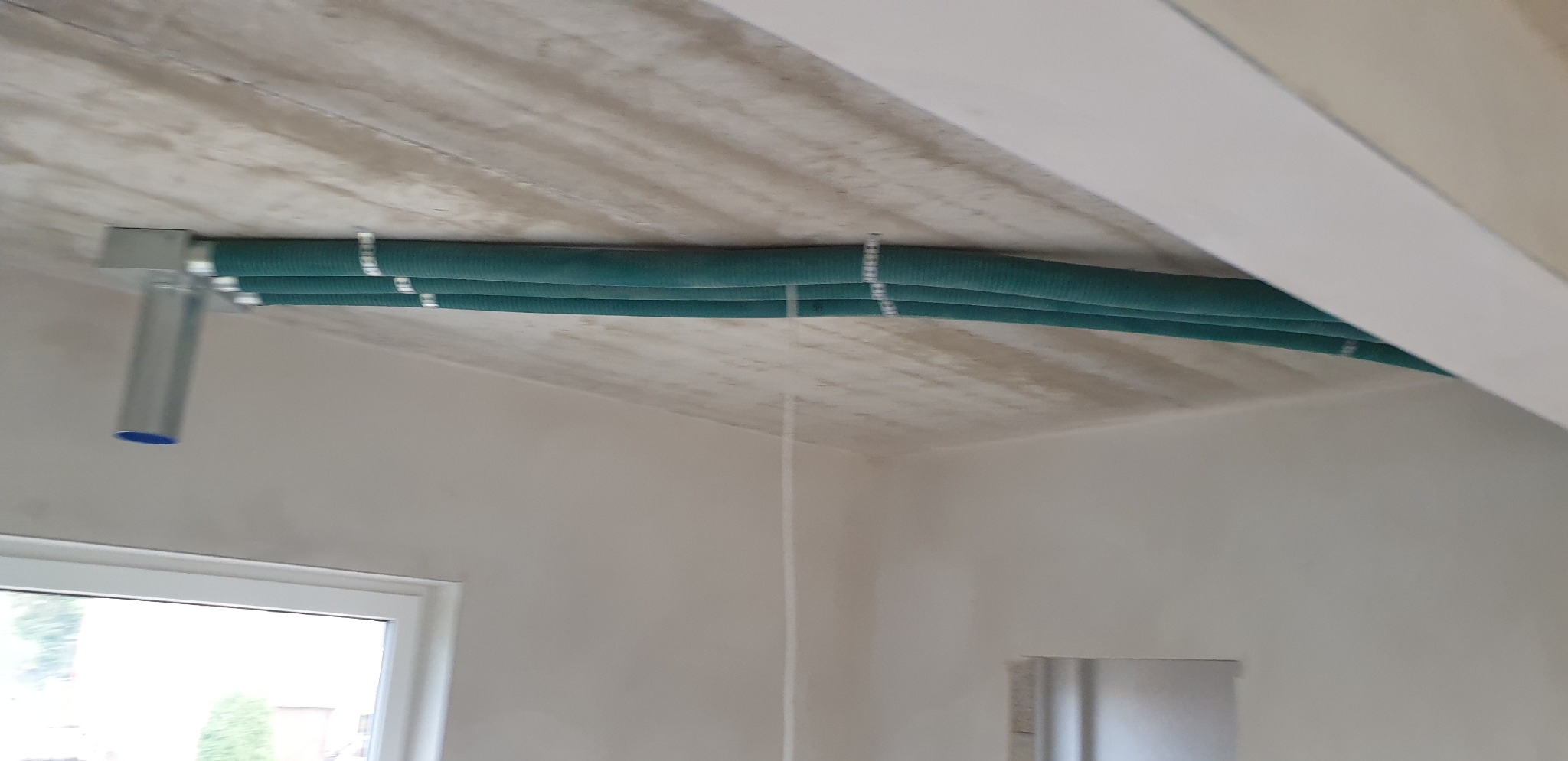 Zielone rury wentylacyjne pod betonowym stropem w nowym domu w Chełmie, widoczne elementy montażowe i fragment okna.