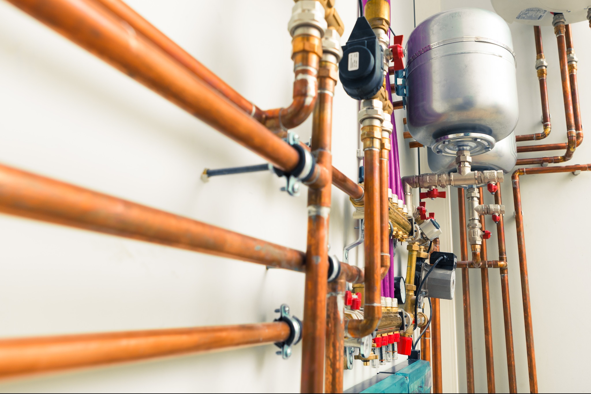 Skomplikowana instalacja z miedzianych rur, zaworów i zbiorników wyrównawczych w Bielsko-Białej, zamontowana na białej ścianie. Widoczne różowe rury i elementy automatyki.