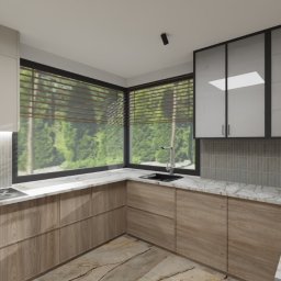 OLIV - Design projektowanie wnętrz Justyna Leszczyńska - Nowoczesna kuchnia z drewnianymi szafkami, marmurowym blatem i dużym oknem z widokiem na zieleń. Minimalistyczny design z akcentem w postaci dekoracyjnej trawy w wazonie.