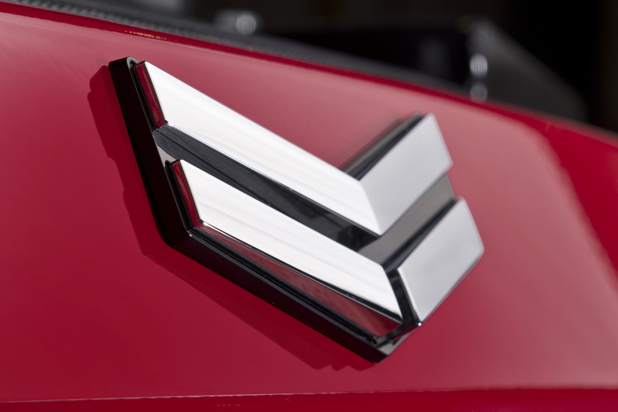 Błyszczący, chromowany emblemat w kształcie strzałek na czerwonym lakierze maszyny budowlanej, widok z bliska.