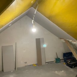 StanBud Michał Stanek - Adaptacja poddasza: surowe ściany po wstępnym wykończeniu, widoczne płyty gotowe do montażu, narzędzia i skrzynka narzędziowa w tle, zabezpieczona folią żółta połać dachu.