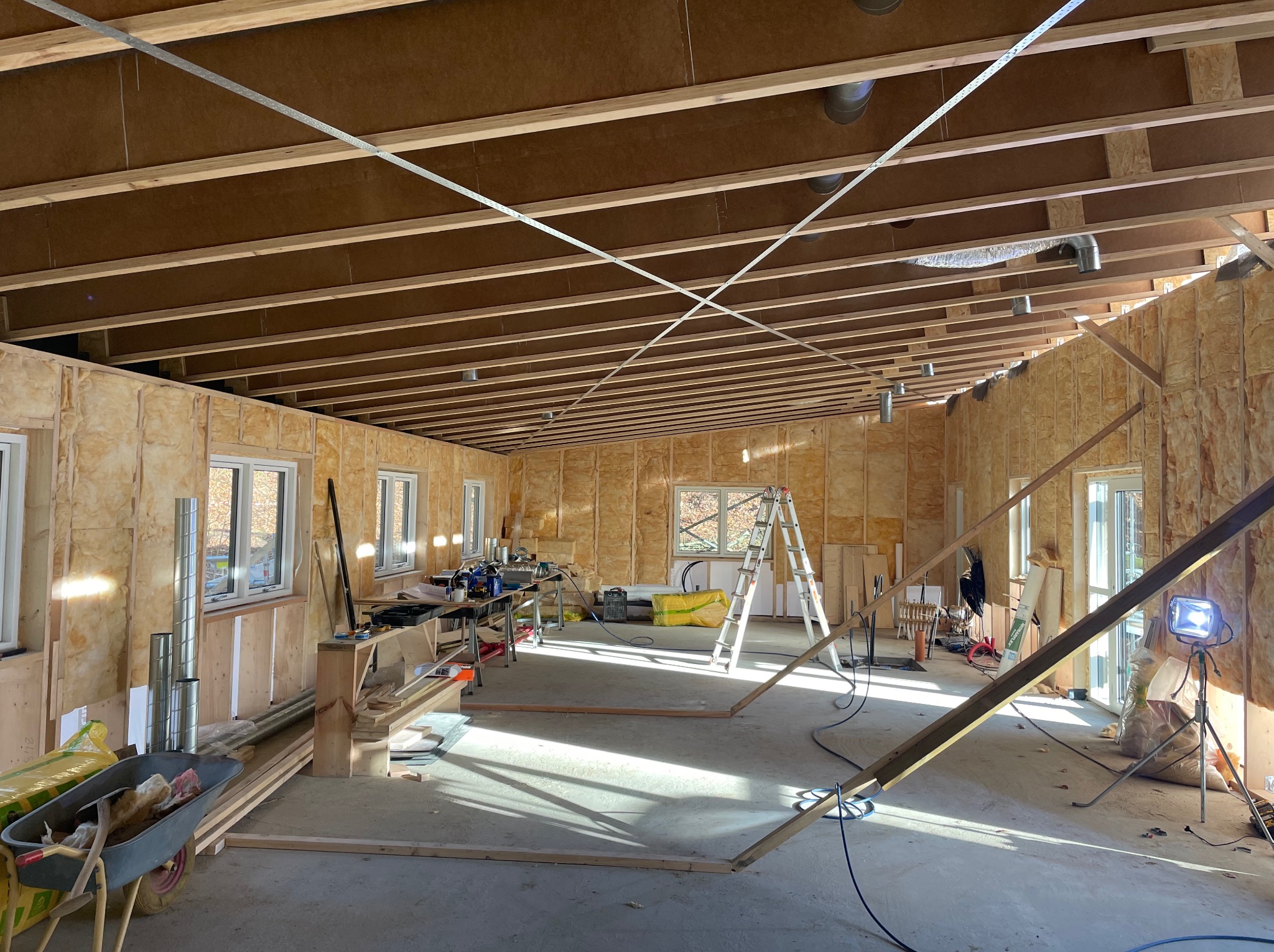 Wnętrze w trakcie wykańczania z widoczną konstrukcją ścian z płyt OSB, drewnianą konstrukcją dachu i rozciągniętymi metalowymi linkami stabilizującymi, narzędzia i materiały budowlane porozrzucane...