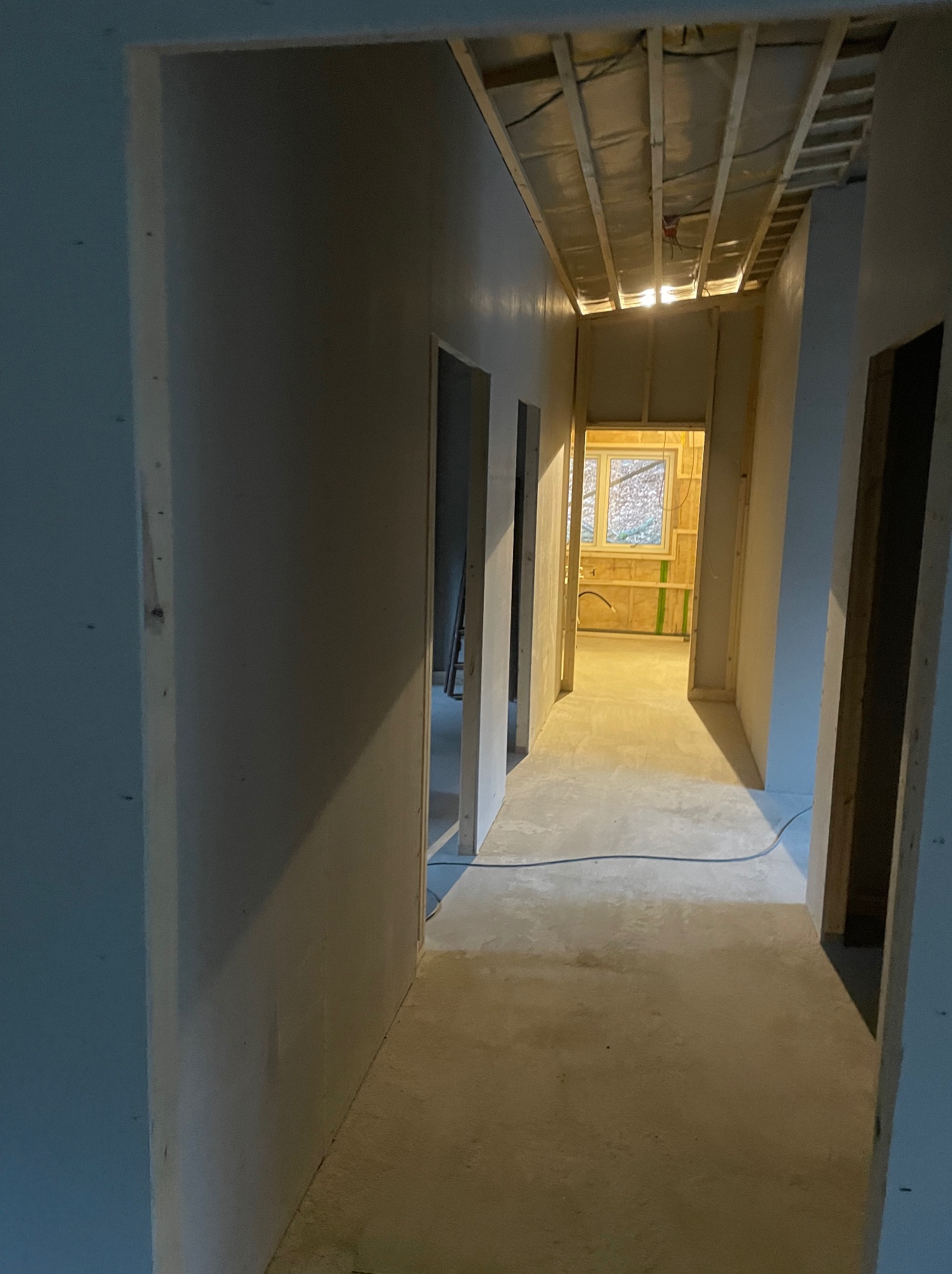 Korytarz w trakcie remontu z widoczną konstrukcją sufitu, ścianami przygotowanymi do dalszych prac wykończeniowych i oknem w oddali.