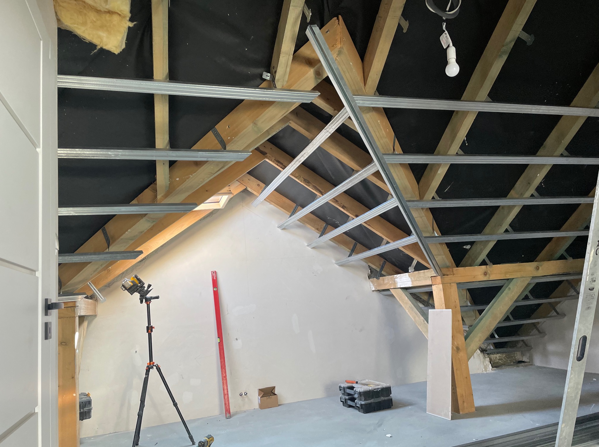 Montaż stelaża z profili metalowych pod płyty karton-gips na poddaszu, widoczny laser krzyżowy na statywie, poziomica i narzędzia.