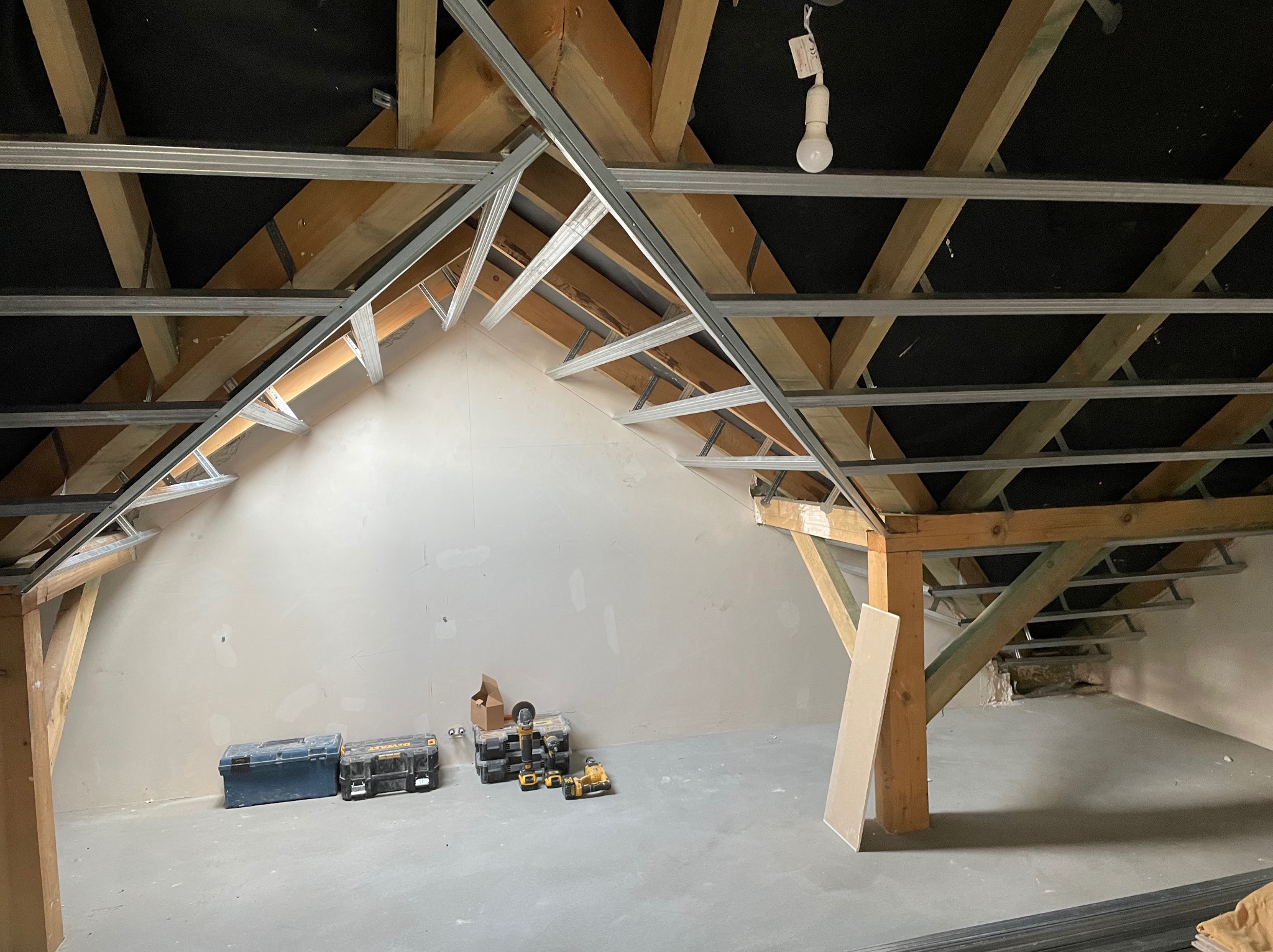 Poddasze w trakcie adaptacji: drewniana konstrukcja dachu z zamontowanymi metalowymi profilami, przygotowanymi pod montaż okładzin. Widoczne narzędzia i materiały budowlane. Ściany wstępnie...