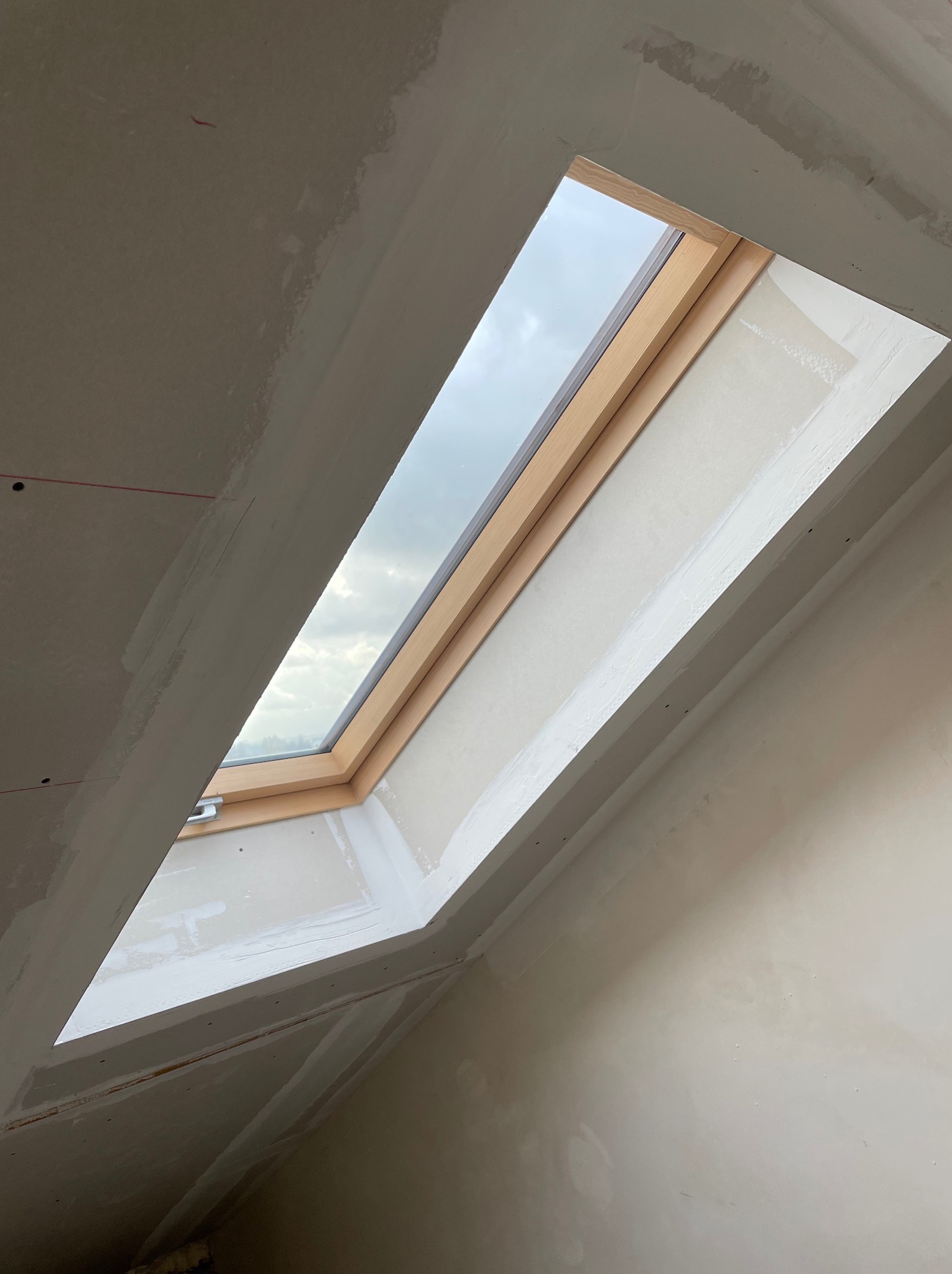 Montaż okna dachowego w skośnym suficie z płyt kartonowo-gipsowych, widoczne łączenia płyt wymagające wykończenia.