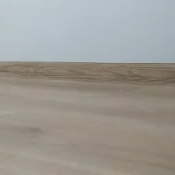 Ułożone panele podłogowe z widoczną listwą przypodłogową przy ścianie w kolorze jasnego beżu.