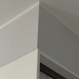 Szare ściany i biały sufit połączone listwą przypodłogową w rogu pokoju, widoczny fragment okna.