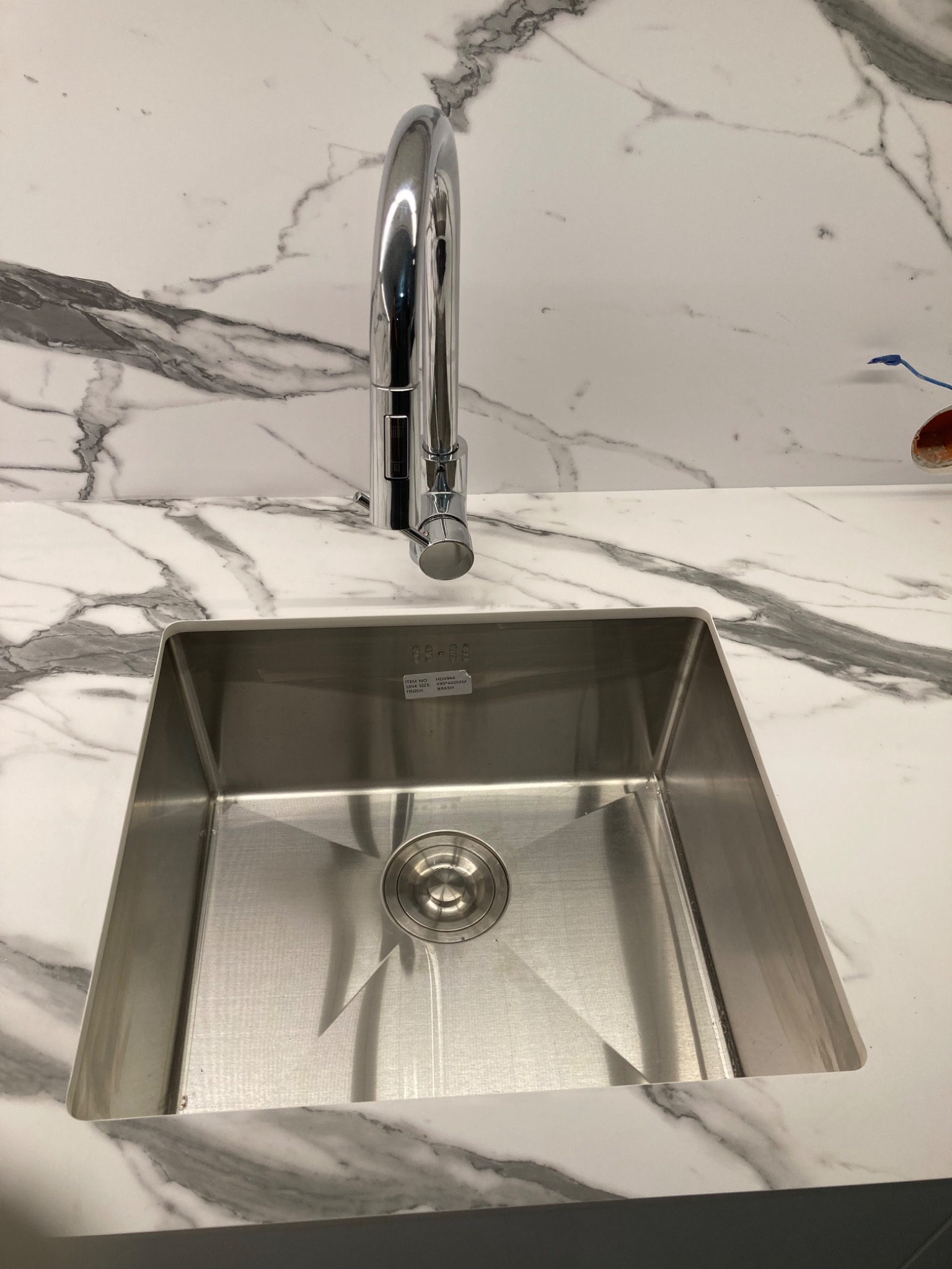 Błyszczący, stalowy zlew kuchenny z chromowaną baterią na blacie z białego marmuru z wyraźnymi szarymi żyłami.