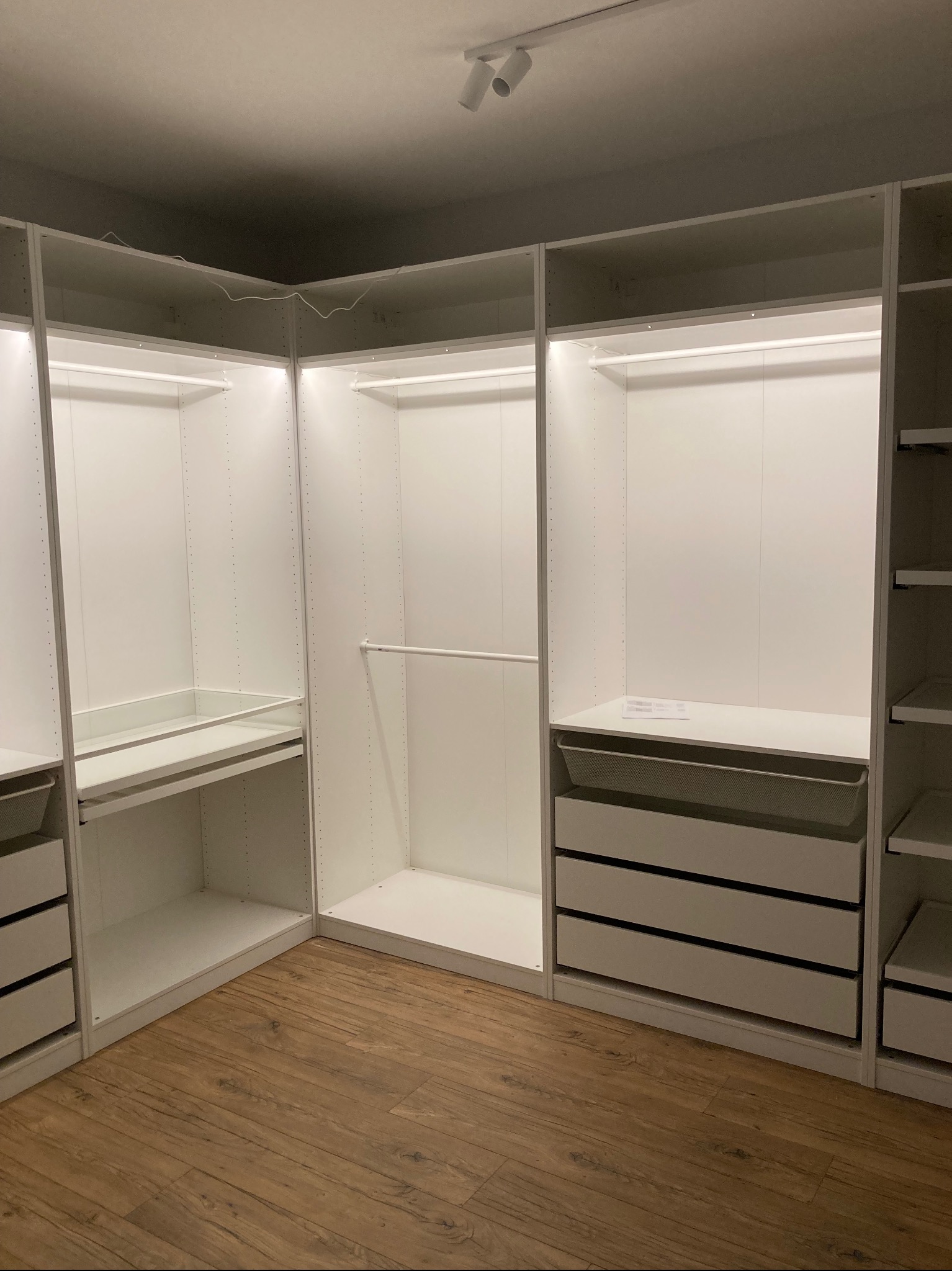 Biała, modułowa garderoba z oświetleniem LED, widok z perspektywy podłogi z paneli, wnętrze szaf puste.