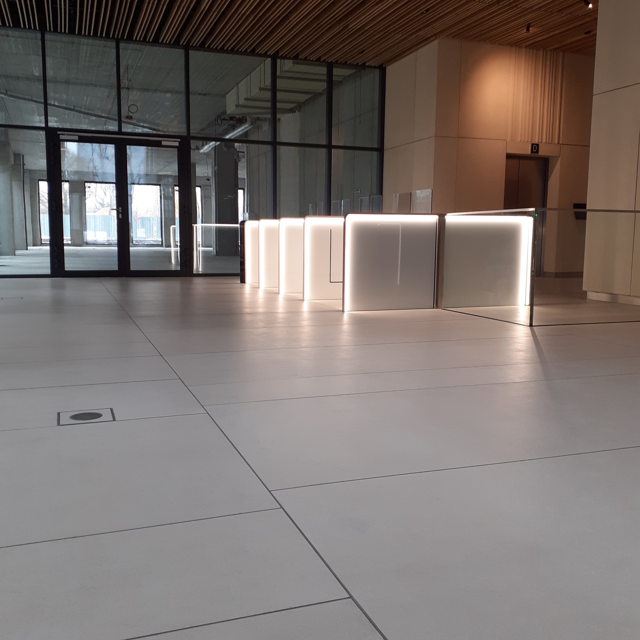 Wykończona posadzka z jasnych, wielkoformatowych płyt w nowym biurze, z widocznymi szklanymi ściankami działowymi i drewnianym sufitem lamelowym.