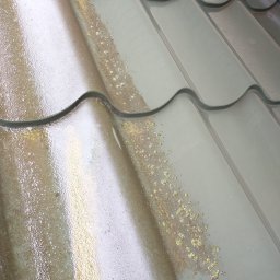 MMI- mycie malowanie impregnacja PAWEŁ LABASZ-GŁOWACKI - Fragment dachu z metalowej blachy dachówkowej, częściowo umyty, z widocznymi śladami mchu i zabrudzeń. Widoczne różnice w czystości powierzchni.