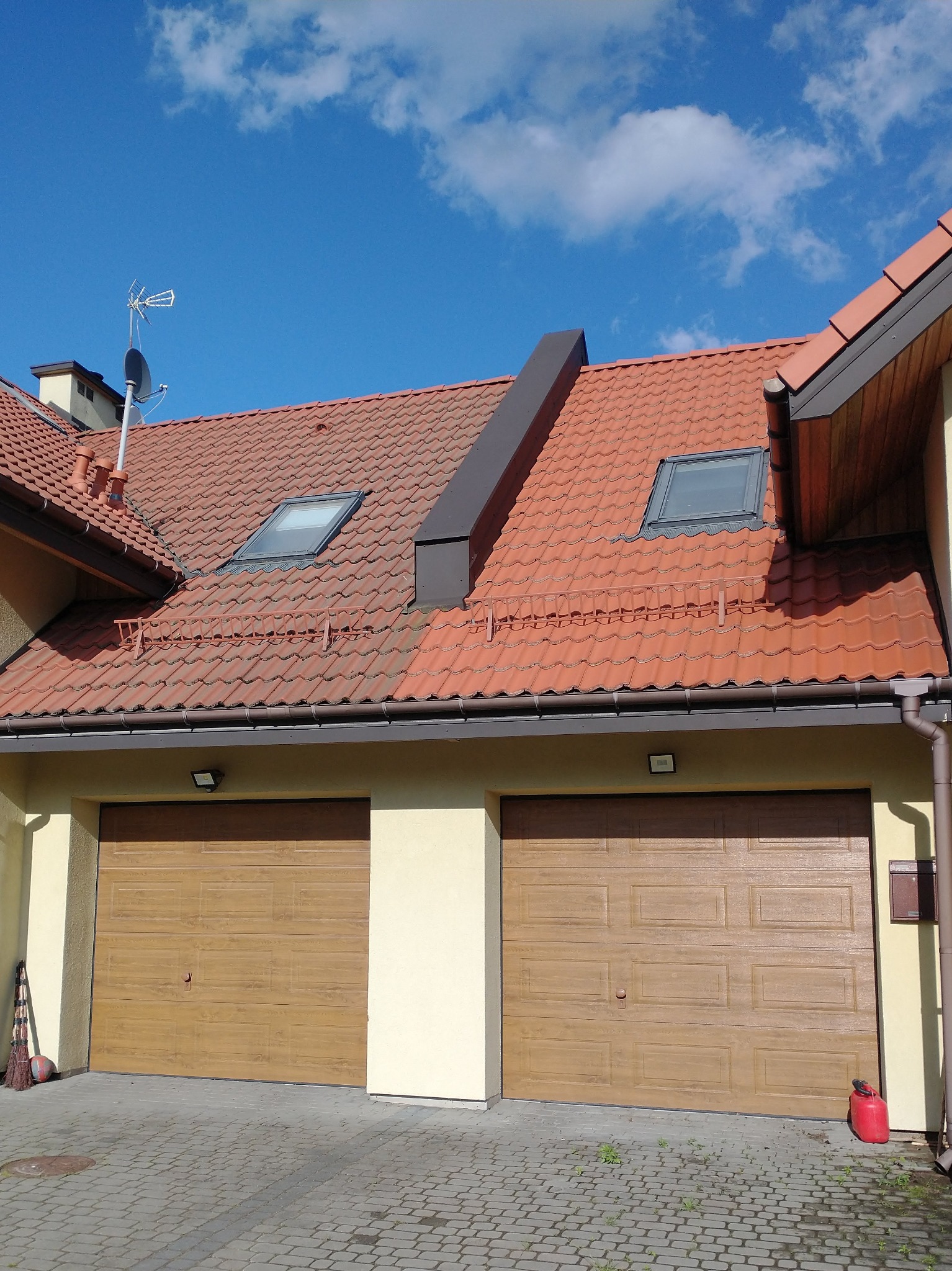 Częściowo umyty dach z czerwonej dachówki z dwoma oknami dachowymi, widoczna różnica w kolorze pomiędzy czystą a brudną częścią dachu, na dole dwa garaże z brązowymi bramami.