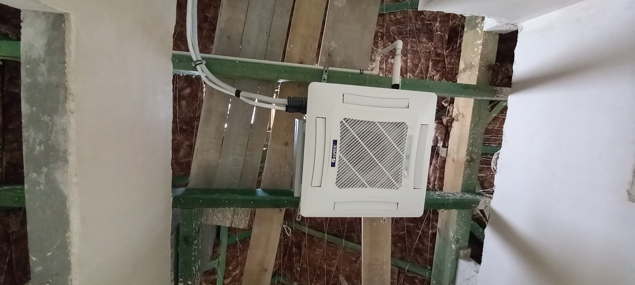 Kasetonowa jednostka klimatyzacji marki Gree zamontowana w suficie podwieszanym z widoczną izolacją i elementami konstrukcyjnymi.