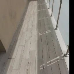 Balkon z nową, jasną podłogą z płytek imitujących drewno, zabezpieczony szklaną balustradą ze stalowymi słupkami, widok z góry.