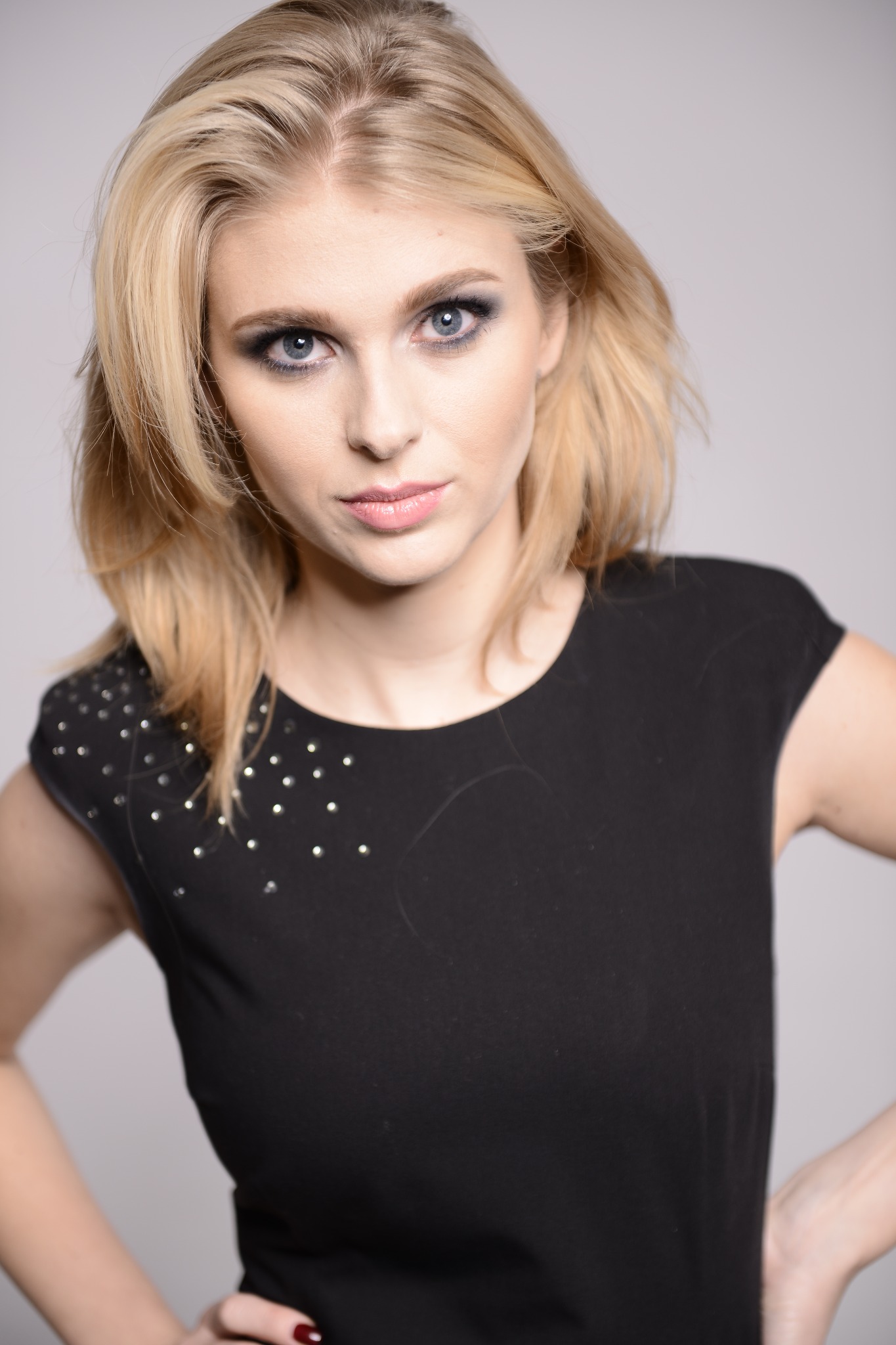 Portret blondynki z intensywnym smoky eye i błyszczącymi ustami, pozującej w czarnej sukience z aplikacjami.