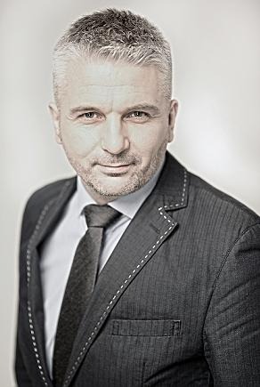 Portret biznesowy mężczyzny w garniturze z ozdobnymi przeszyciami, na jasnym tle.