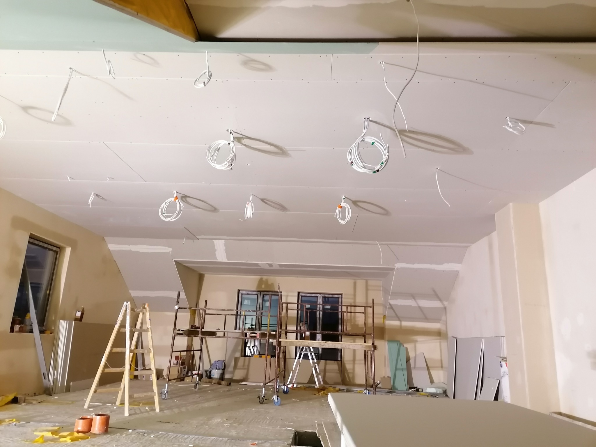 Montaż sufitu podwieszanego z płyt gipsowo-kartonowych, widoczne kable elektryczne, rusztowania i drabina.