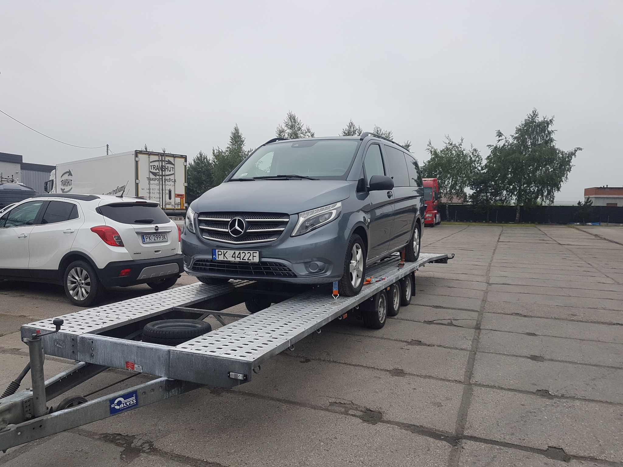 Szary Mercedes Vito na perforowanej, metalowej lawecie z zapasowym kołem, z widoczną tablicą rejestracyjną PK 4422F, na betonowym placu postojowym, obok zaparkowany biały Opel Mokka z tablicą PK...