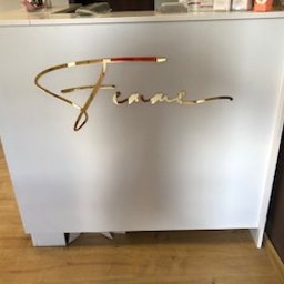 ART-REKLAMA - Biała lada recepcyjna z dekoracyjnym, złotym napisem 'Femme' wykonanym z błyszczącego materiału, ustawiona na drewnianej podłodze w jasnym wnętrzu.