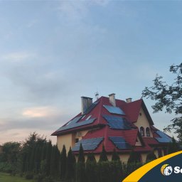 Solday - Dom jednorodzinny z panelami słonecznymi na czerwonym dachu, widok z ogrodu w pochmurny dzień, logo firmy w prawym dolnym rogu.