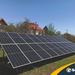 Solday - Panel słoneczny na trawniku przed domem z czerwoną dachówką w słoneczny dzień.