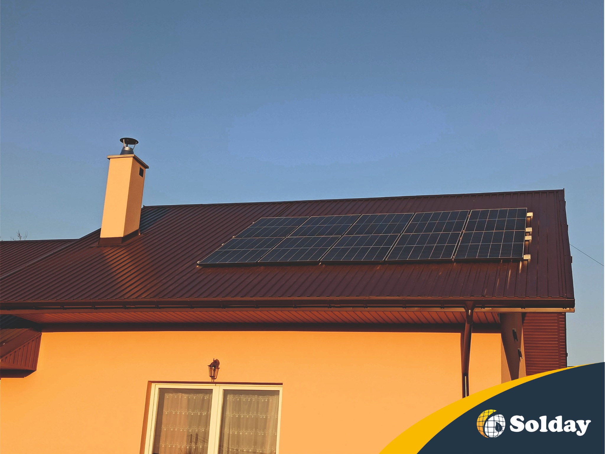 Panel słoneczny zamontowany na brązowym dachu domu z beżową elewacją, widoczny komin i fragment okna, na dole logo firmy.
