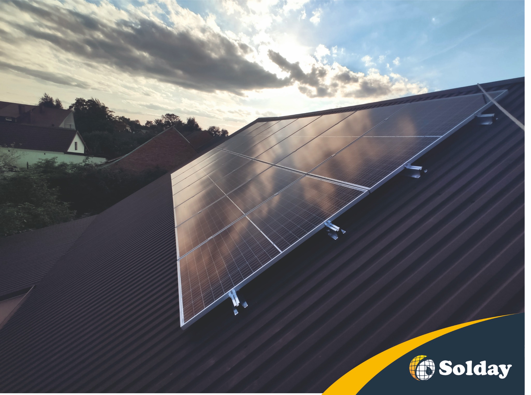 Panele słoneczne na brązowym dachu blachodachówkowym, z widocznym logotypem firmy Solday w prawym dolnym rogu i pochmurnym niebem w tle.