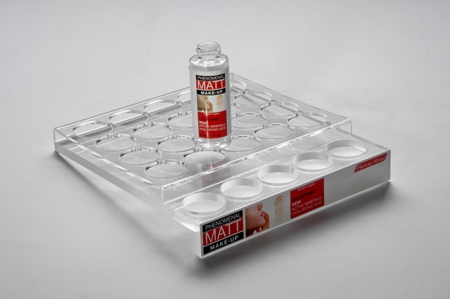 Przezroczysty akrylowy ekspozytor z okrągłymi wgłębieniami, prezentujący butelkę kosmetyku 'Phenomenal Matt Make-up' z etykietą informującą o składnikach aktywnych i logo producenta 'Pierre Rene'.